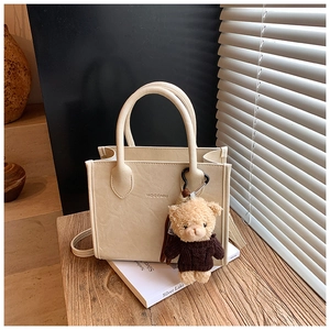 Detail of a vintage cream leather tote bag featuring a cute brown plush bear charm