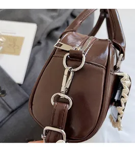 Detail of silver metallic buckles and D-ring on a brown glossy leather shoulder bag