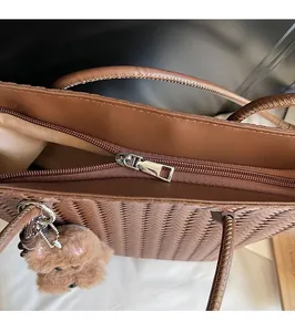 Detail of a brown woven tote bag featuring a smooth metal zipper and a cute teddy bear charm