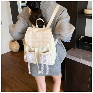 Detail of cream backpack featuring plaid flap and decorative white lace ribbons