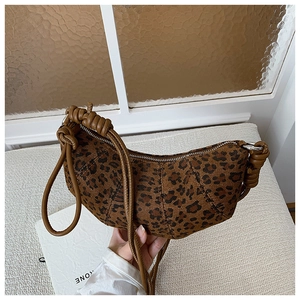 Close-up of leopard print crescent bag featuring woven leather knotted shoulder strap