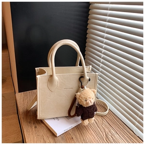 Detail of cream-colored tote bag with lychee texture and cute bear pendant on wood surface