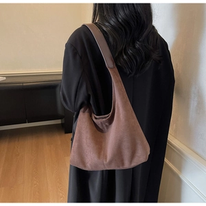 Detail of a large vintage brown suede hobo bag worn by a model in a minimalist room