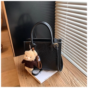 Detail of black leather tote bag with natural texture, round handles and bear charm