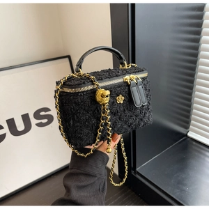 Detail of black tweed box bag featuring golden flower accent and chain strap