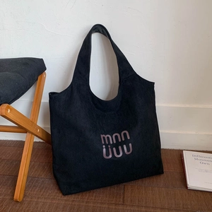 Detail of black suede tote bag with purple lettering logo on a dark wood floor