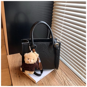 Close-up of black leather tote bag with lychee texture and cute teddy bear charm