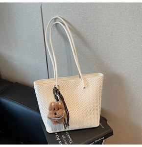 Close-up of a white woven tote bag featuring a cute brown dog plush charm and ribbon decor
