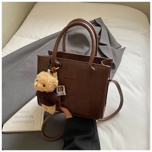 Close-up of retro dark brown leather handbag featuring a cute plush bear charm accessory
