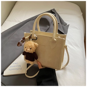 Detail of a beige faux leather tote bag with MOCOMU logo and cute teddy bear charm