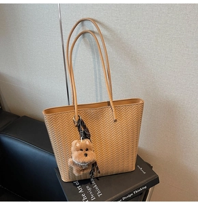 Detail of tan woven tote bag with herringbone texture and a brown plush puppy charm
