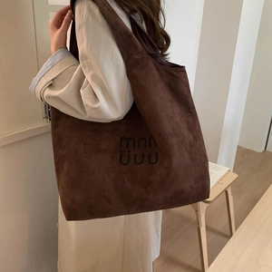 Detailed close-up of dark brown suede tote bag with embossed logo and wide shoulder strap