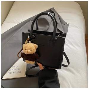 Detail of black PU leather tote with brand logo and brown teddy bear charm accessory