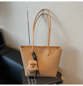 Detail of light brown woven tote bag featuring slender straps and a cute plush dog pendant