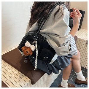 Detail view of black leather Boston bag with suede panels and a cute teddy bear charm