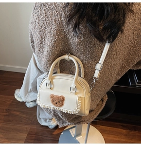 Detail der cremefarbenen Boston-Tasche mit Plüschbären-Charm und Spitzenbesatz-Akzenten
