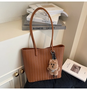 Detail of brown woven tote bag with herringbone pattern and cute plush doll pendant