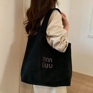 Detailed view of the large black corduroy tote bag with pink logo embroidery on shoulder