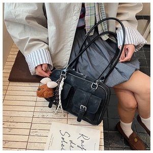 Close-up of vintage black suede shoulder bag with dual flap pockets and a cute bear charm