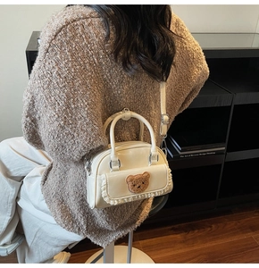 Detail of cream patent leather mini bag featuring plush bear patch and delicate lace trim