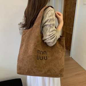 Brown suede tote bag with logo detail shown from a side-back view on shoulder