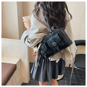 Detail of black suede Boston bag featuring dual front pockets and a cute bear charm