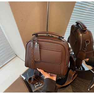 Detail view of brown lychee grain leather crossbody bag with wide strap and rivet tags