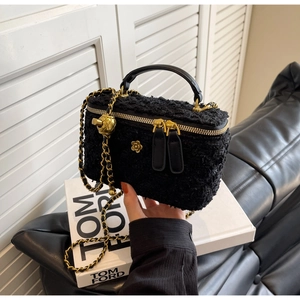 Macro shot of black tweed vanity bag with gold floral logo and woven chain strap