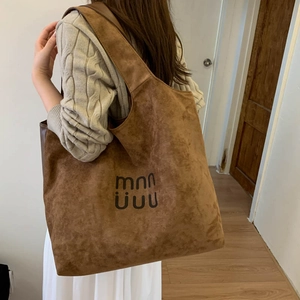 Detail of a brown suede tote bag with black letter logo shown on a model's shoulder