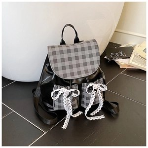 Detail of black backpack with plaid flap and large white lace bows in a lifestyle setting