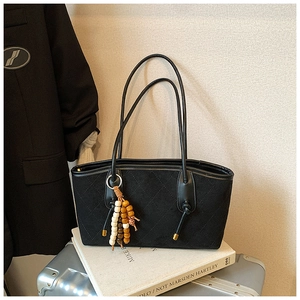 Close-up of black suede underarm bag with quilted stitching and vintage wooden bead pendant