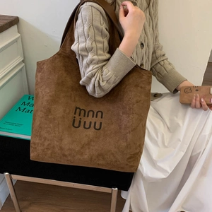 Detail of a brown suede tote bag with black artistic logo mnn uuu in a lifestyle setting