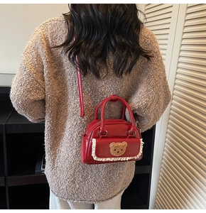 Detail der roten Lackledertasche mit Plüschbär-Patch und weißer Spitzenborte