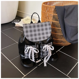 Close-up of plaid fabric flap and delicate white lace bows on a black leather backpack