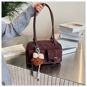 Detail of dark burgundy suede handbag featuring double pockets and cute plush bear charm