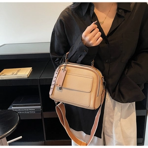 Detail of apricot pebbled leather crossbody bag with wide strap and decorative tags
