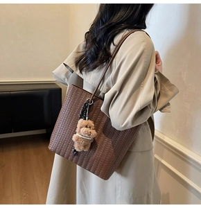 Detail of dark brown woven tote bag with leather straps and cute bear charm accessory