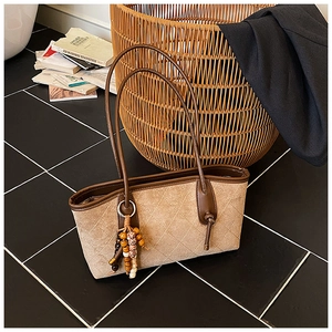 Close-up of quilted suede tote bag featuring vintage brown straps and a wooden bead tassel