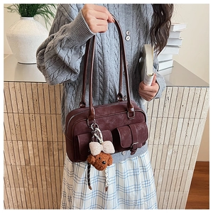 Detail of burgundy suede Boston bag with flap pockets and a cute teddy bear pendant