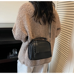 Detail of black lychee grain leather bag with rivets, zippers and long pullers in home setting