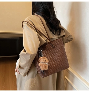 Dettaglio della borsa tote intrecciata marrone con ciondolo a orsetto su un trench lungo