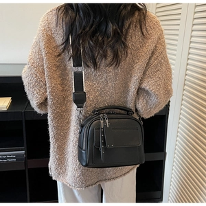 Detail view of black lychee grain leather crossbody bag with wide striped fabric strap on model
