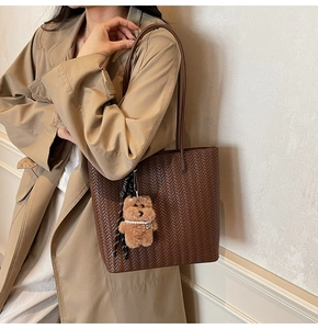 Dettaglio borsa tote intrecciata marrone scuro con ciondolo a orsetto su trench autunnale