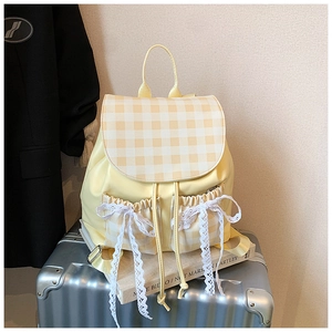 Detail view of yellow backpack with plaid pattern flap and white lace bow decoration