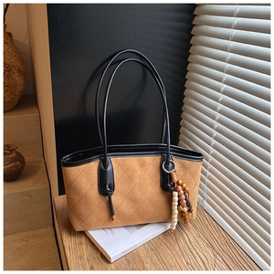 Detailed close-up of brown quilted faux suede tote bag with vintage bead pendant