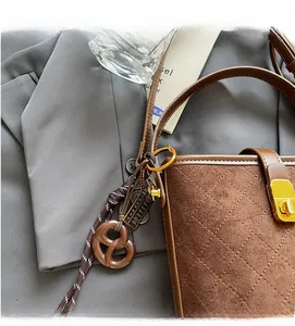 Detail of brown suede bucket bag with quilted stitching and decorative tassel charm