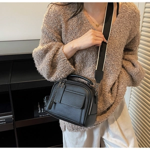 Close-up of black lychee grain leather crossbody bag with metal rivets and wide strap