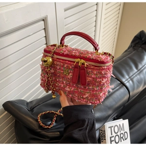 Close-up of pink tweed box bag with gold floral ornament and red leather handle