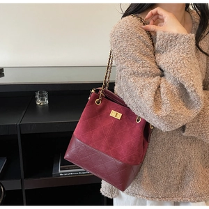 Close-up of burgundy suede bucket bag with quilted patterns and metal chain strap