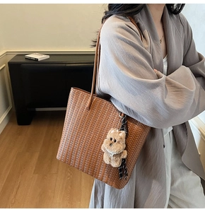 Dettaglio di una borsa tote intrecciata marrone con un ciondolo a forma di orsetto